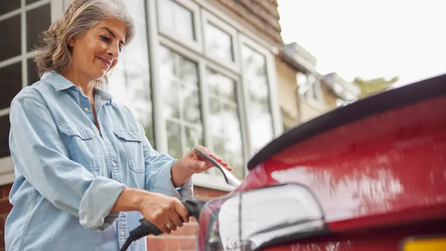 middle aged woman charging an electric car